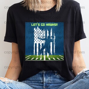 May include: Black t-shirt with a graphic of a football player throwing a football in front of an American flag with the text "LET'S GO HAWKS!"