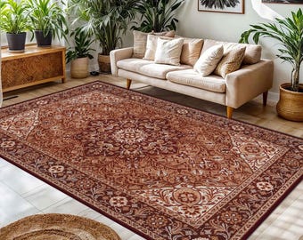 May include: A large, rectangular area rug with an ornate, traditional design. The rug features a deep burgundy background with intricate patterns in shades of cream, tan, and brown. The rug is placed in a living room setting with a sofa and plants.