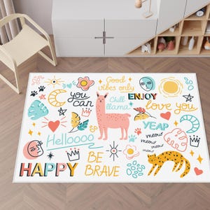 May include: A white rug with colorful illustrations of a llama, a cat, a sun, a moon, hearts, stars, and crowns. The rug has the text "You can", "Good vibes only", "Chill llama", "Enjoy", "Love you", "Yeap meow meow meow meow", "Helloooo", "Be brave", and "Happy" on it.