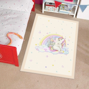 Può includere: Un tappeto bianco e crema con un'illustrazione ad acquerello di un unicorno seduto su una nuvola con un arcobaleno e un castello sullo sfondo. Il tappeto è decorato con piccole stelle rosa, blu e gialle.