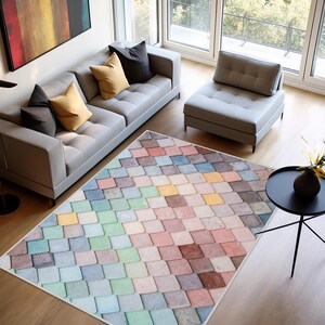 May include: A multi-coloured rug featuring a geometric design of squares in pastel shades of blue, green, pink, yellow, and brown. The rug is on a wooden floor in a living room, with a grey sofa and chair.