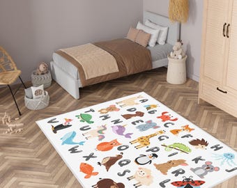 May include: A white rectangular children's rug featuring the alphabet and colorful cartoon animals. The rug is placed on a wooden floor in a bedroom setting, with a bed and other furniture visible in the background.