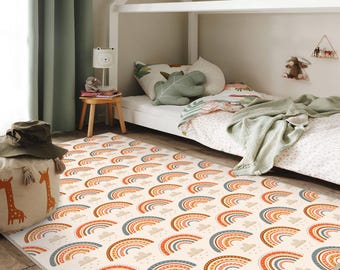 May include: A rectangular area rug featuring a repeating pattern of rainbows and small clouds on a cream background. The rainbows are rendered in shades of orange, terracotta, and muted blue, with dotted and striped textures within each arch.