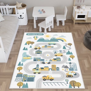 May include: A white play mat with a grey road winding through a city scene. The mat features a hot air balloon, a rainbow, a sun, trees, buildings, and vehicles. The text "William's Map" is printed at the top of the mat.
