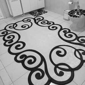 May include: A black and white bathroom rug with a decorative scroll design. The rug is rectangular with a light-colored center and a dark, swirling border. The bathroom also includes a matching toilet seat cover and a small rug.