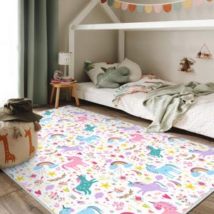 Può includere: Un tappeto rettangolare bianco con un motivo di unicorni colorati. Il tappeto presenta unicorni rosa, blu e turchese, arcobaleni, stelle e motivi floreali. Il tappeto è in una cameretta.