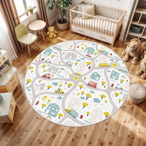 Könnte beinhalten: Runder Kinderteppich mit Stadtkarten-Design. Der Teppich hat einen weißen Hintergrund mit grauen Straßen, Häusern, Bäumen und verschiedenen Fahrzeugen in Rot, Gelb und Blau. Geeignet für ein Kinderzimmer oder Spielzimmer.