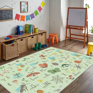 Op de afbeelding: Een lichtgroen educatief tapijt met insectenillustraties en het alfabet. Het tapijt ligt in een kinderspeelkamer met een houten opbergmeubel, een whiteboard en kleurrijke decoraties. Het tapijt meet ongeveer 152 cm bij 203 cm.