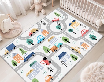 May include: A rectangular area rug featuring a white background with a printed road network, colorful cartoon houses, various vehicles including cars and trucks, and green trees. The design includes a circular roundabout and winding paths.