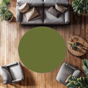 May include: Overhead view of a living room with a large olive green round rug. The rug is centered on a wooden floor, surrounded by a gray sofa, two armchairs, and a small wooden coffee table. Potted plants add greenery.