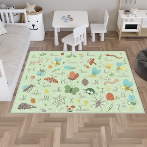Op de afbeelding: Een lichtgroen kinderkleed met een alfabet en insectenillustraties. Het kleed heeft een wit stippenpatroon en bevat afbeeldingen van mieren, bijen, vlinders en spinnen. De letters van het alfabet worden ook weergegeven.