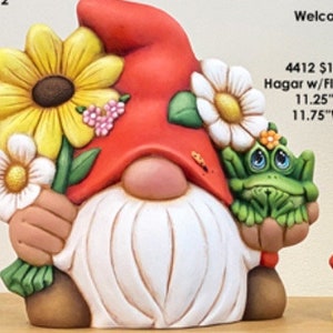 May include: Ceramic gnome figurine with a red hat, white beard, and holding a bouquet of yellow and white flowers. A green frog sits on the gnome's other hand. The gnome is 11.25 inches tall and 11.75 inches wide.