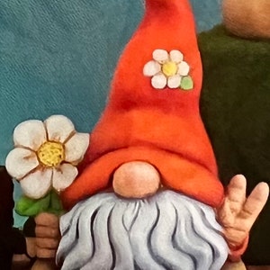 May include: A ceramic gnome figurine with a red hat, white beard, and a white flower on its hat. The gnome is holding a white flower in its hand and has a peace sign on its other hand.