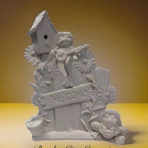 May include: White ceramic figurine of a welcome sign with two frogs, one playing a guitar and the other sitting on a log. The sign is decorated with flowers and a birdhouse.