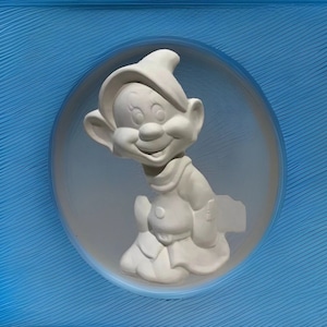 May include: A white ceramic figurine of a dwarf with a pointed hat and a friendly smile. The figurine is set against a blue background.