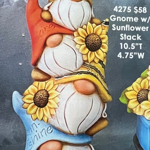 May include: A stack of three gnomes with sunflower hats. The top gnome has a red hat with the word "are" written on it. The middle gnome has a yellow and black striped hat. The bottom gnome has a blue hat with the words "sun-shine" written on it. The gnomes are 10.5 inches tall and 4.75 inches wide.