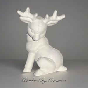 May include: A white ceramic reindeer figurine in a seated position. The reindeer has large antlers and a detailed, textured surface. The figurine is unpainted and ready for customization. The text "Border City Ceramics" is at the bottom.
