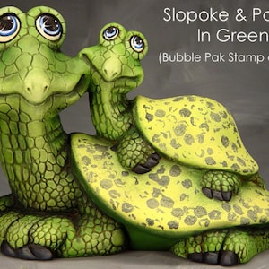 May include: A whimsical green turtle sculpture with a smaller turtle on its back. The turtles have large, expressive eyes with blue and white highlights. The text "Slopoke & Pokey In Green" is visible.