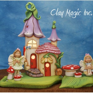 May include: A whimsical fairy house with a pink flower roof, a red door, and two fairies with wings. The house is surrounded by green grass and mushrooms.