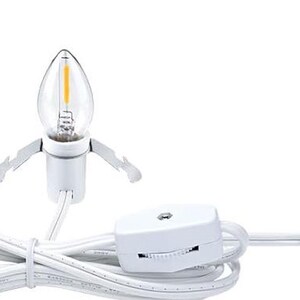 May include: A white candelabra bulb with a clear, teardrop-shaped glass and a warm yellow filament. The bulb is connected to a white cord with a dimmer switch and a two-pin plug.