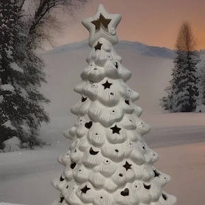 May include: White ceramic Christmas tree with cut-out stars, hearts, and moons. The tree has a star on top and is sitting on a snowy surface.  Border City Ceramics.