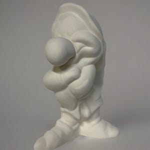 May include: White ceramic figurine of a gnome with a large nose and a hat. The gnome is standing with its arms crossed and is looking down.
