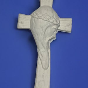 May include: White ceramic cross with a sculpted image of Jesus's head with a crown of thorns. The cross is on a blue background.  Border City Ceramics.