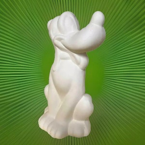 May include: White ceramic figurine of a cartoon dog with floppy ears and a big smile. The dog is sitting with its head tilted to the side and its right paw raised.