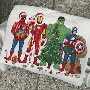 Puede incluir: Sudadera blanca con un diseño navideño con Spider-Man, Iron Man, Hulk y Capitán América con gorros de Papá Noel. Los superhéroes están rodeados de decoraciones navideñas, incluyendo un árbol y regalos.