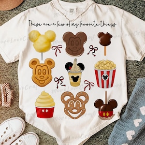 May include: White t-shirt featuring various cartoon food illustrations, including a Mickey Mouse-shaped waffle, caramel apple, and popcorn. The text "These are a few of my favorite things" is printed across the top. A fun, whimsical design.