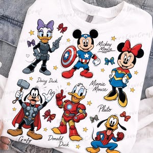 May include: White sweatshirt featuring cartoon characters Daisy Duck, Mickey Mouse, Minnie Mouse, Goofy, Donald Duck, and Pluto dressed as superheroes. The design includes stars, bows, and character names. The text "More Love Craft" is also visible.