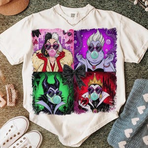 May include: White t-shirt featuring four cartoon portraits of Disney villains, each blowing a bubblegum bubble and wearing heart-shaped sunglasses. The villains are Cruella de Vil, Ursula, Maleficent, and the Evil Queen.
