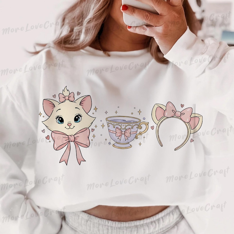 May include: White sweatshirt featuring three cartoon illustrations: a cat with a pink bow, a teacup with a pink bow, and a headband with cat ears and a pink bow. The design includes hearts and stars.