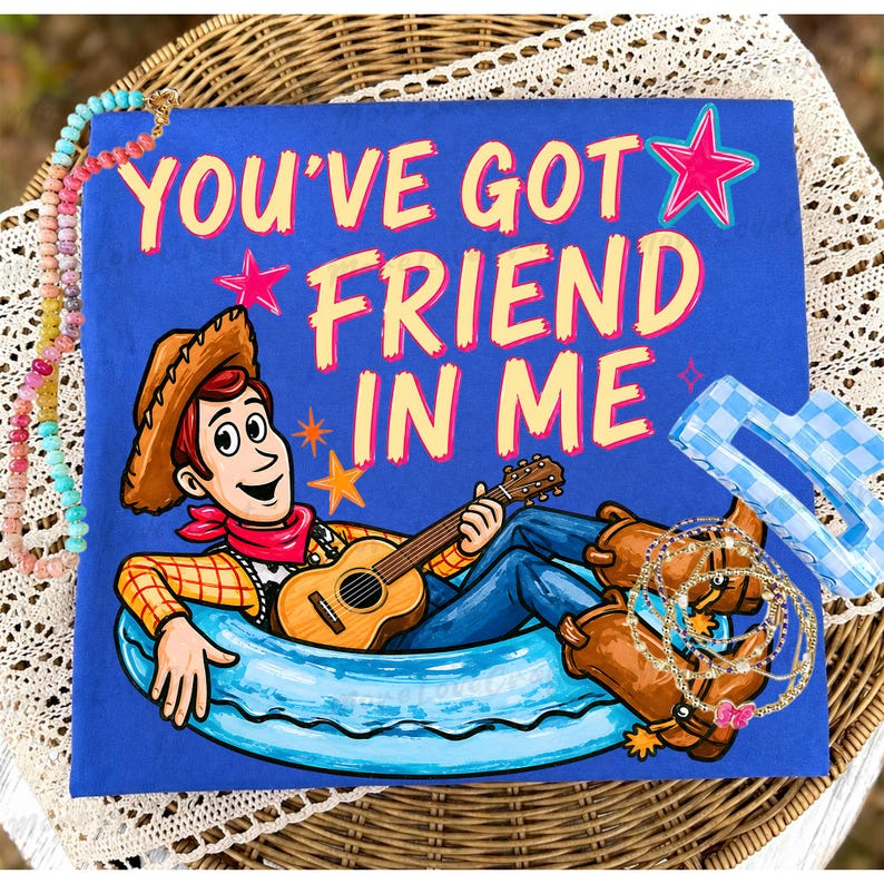 May include: A blue t-shirt with the phrase "YOU'VE GOT A FRIEND IN ME" in yellow and pink. The shirt features a cartoon cowboy playing a guitar. Accessories include bracelets and a blue checkered hair clip.