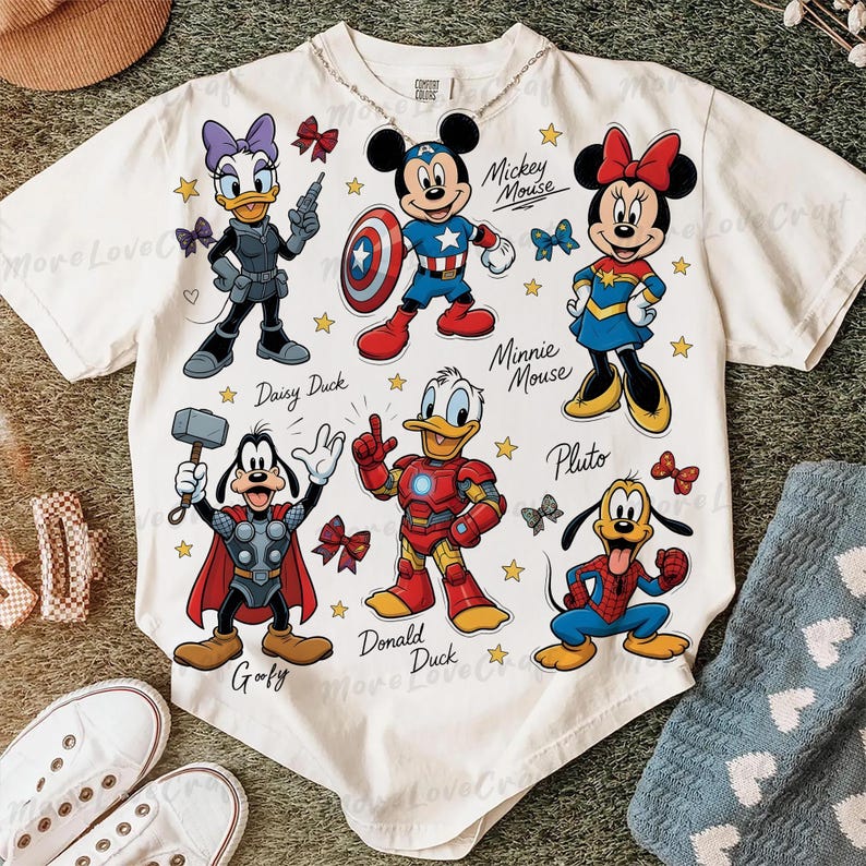 May include: White short-sleeved bodysuit featuring cartoon characters Mickey Mouse, Minnie Mouse, Donald Duck, Daisy Duck, Goofy, and Pluto in superhero costumes. The design includes stars and bows, with character names below.