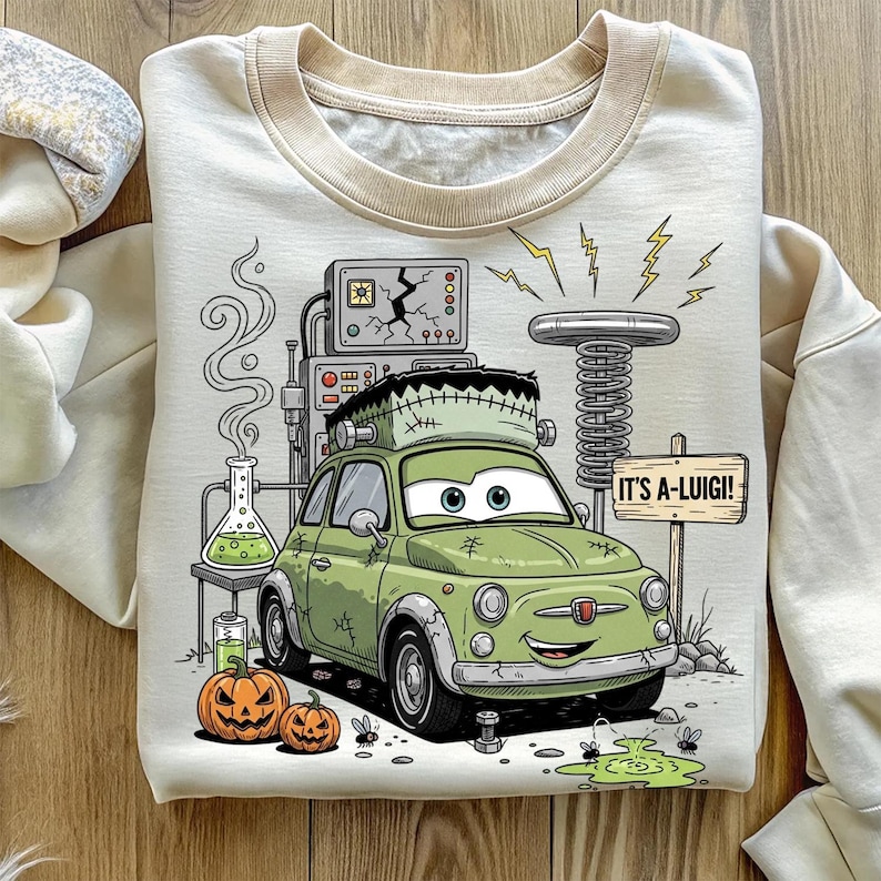 Puede incluir: Sudadera crema con un coche verde de dibujos animados con rasgos de Frankenstein. El dise&ntilde;o incluye una escena de laboratorio, calabazas, rayos y el texto "IT'S A-LUIGI!"