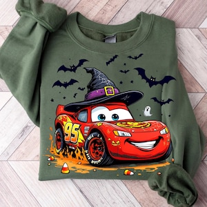 Puede incluir: Sudadera verde con un coche de dibujos animados de Rayo McQueen con un sombrero de bruja. El coche rojo tiene el n&uacute;mero 95 y llamas. Murci&eacute;lagos, estrellas, un fantasma y caramelos de ma&iacute;z tambi&eacute;n est&aacute;n en el dise&ntilde;o.