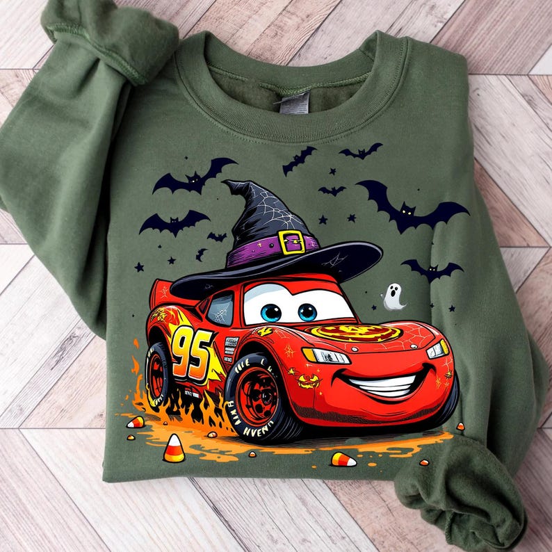 Puede incluir: Sudadera verde con un coche de dibujos animados de Rayo McQueen con un sombrero de bruja. El coche rojo tiene el n&uacute;mero 95 y llamas. Murci&eacute;lagos, estrellas, un fantasma y caramelos de ma&iacute;z tambi&eacute;n est&aacute;n en el dise&ntilde;o.