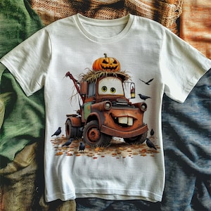 Puede incluir: Camiseta blanca con un dise&ntilde;o de cami&oacute;n de remolque de dibujos animados, coronada con una calabaza tallada. El cami&oacute;n es marr&oacute;n con una cara sonriente y dientes grandes. Cuervos negros y hojas de oto&ntilde;o rodean el cami&oacute;n.