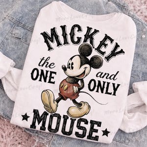 May include: White sweatshirt featuring a graphic of Mickey Mouse with the text "MICKEY the ONE and ONLY MOUSE". The cartoon character is in a walking pose, wearing red shorts and yellow shoes. The text is in a bold, black font.