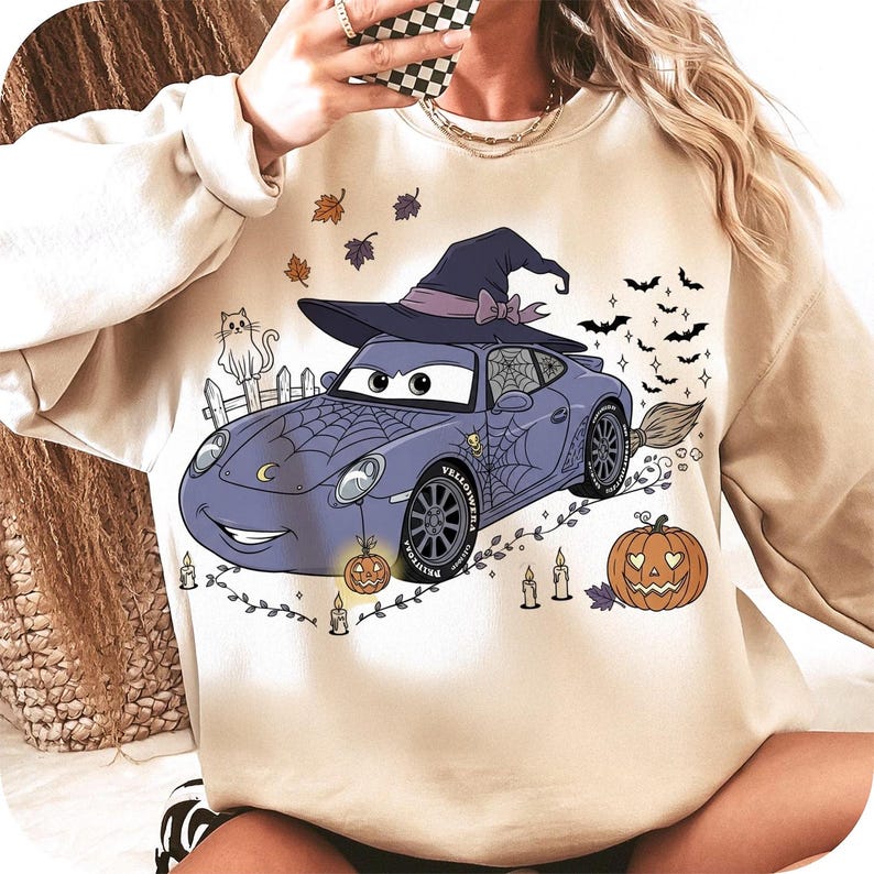 Puede incluir: Sudadera beige con un dise&ntilde;o de coche de dibujos animados con tem&aacute;tica de Halloween. El coche lleva un sombrero de bruja y est&aacute; decorado con telara&ntilde;as, calabazas, murci&eacute;lagos y velas. Tambi&eacute;n se incluye un gato de dibujos animados en el dise&ntilde;o.