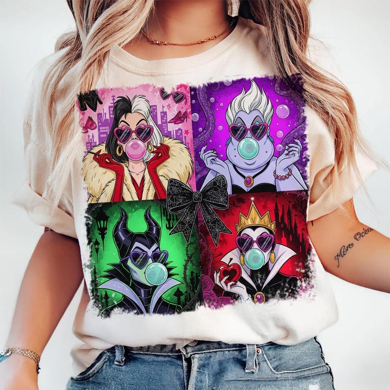 May include: Cream-colored t-shirt featuring a colorful graphic of four Disney villains: Cruella, Ursula, Maleficent, and the Evil Queen. Each character is wearing heart-shaped sunglasses and blowing a bubble. A black bow is in the center.