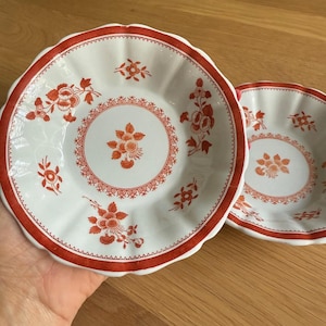 May include: Two white ceramic bowls with red floral designs. The bowls have a scalloped edge and a white background with red floral patterns.