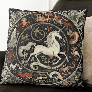 Könnte beinhalten: Ein schwarzes Kissen mit einem weißen Einhorn und anderen Fabelwesen in einem kreisförmigen Design. Der Hintergrund ist schwarz mit goldenen und roten Akzenten.