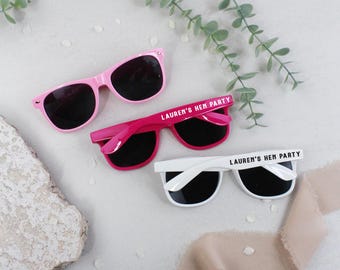 May include: Three pairs of sunglasses with the text "Lauren's Hen Party" printed on the arms. The sunglasses are pink, fuchsia, and white.
