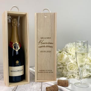 May include: Two wooden champagne bottle gift boxes, one containing a Bollinger champagne bottle. The other box is engraved with "MR & MRS Harrison" and the date "09.09.2026". A bouquet of white roses and a champagne flute are also in the image.