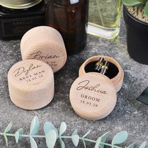 May include: Three wooden boxes with engraved text. The boxes are labelled "Dylan Best Man 18.05.26", "Brian", and "Joshua Groom 18.05.26". One box contains a pair of cufflinks.