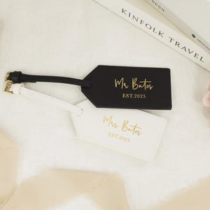May include: Two luggage tags, one black and one white, with gold lettering. The black tag says "Mr. Bates EST. 2025" and the white tag says "Mrs. Bates EST. 2025".