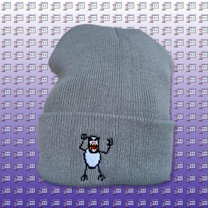 Puede incluir: Gorro de punto gris con un pequeño diseño bordado de una criatura blanca con contorno negro y expresión de enfado. La criatura tiene dos brazos levantados en el aire.