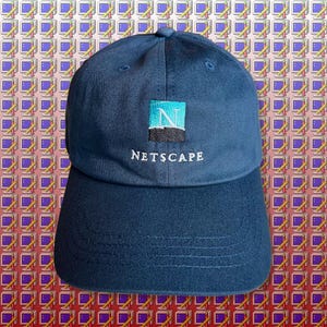 Peut inclure: Une casquette de baseball bleu foncé avec un logo brodé blanc qui dit "Netscape" et un graphique bleu et turquoise de la lettre "N".